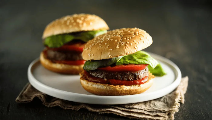 Zwei Hamburger auf einem weißen Teller, belegt mit einer leckeren Sauce, Salat, Tomaten und Ketchup. Das perfekte Hamburger Rezept 