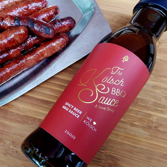 Zooze The Kölsch BBQ Sauce - Beer BBQ Sauce 260ml liegt auf einem Tisch neben Bratwürsten